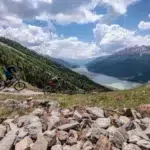 Two cyclists ride the Reschensee scenic tour, enjoying views of the lake and far-off mountain peaks.
