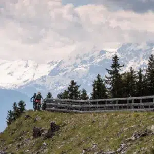 Two cyclists ride along the Uina Gorge Trail, with snow-covered mountain peaks behind them.