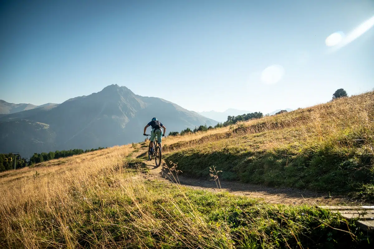 Mountainbiketour Grenzenlos auf einem Feldweg mit grasbewachsenen Hügeln und Bergen im Hintergrund.