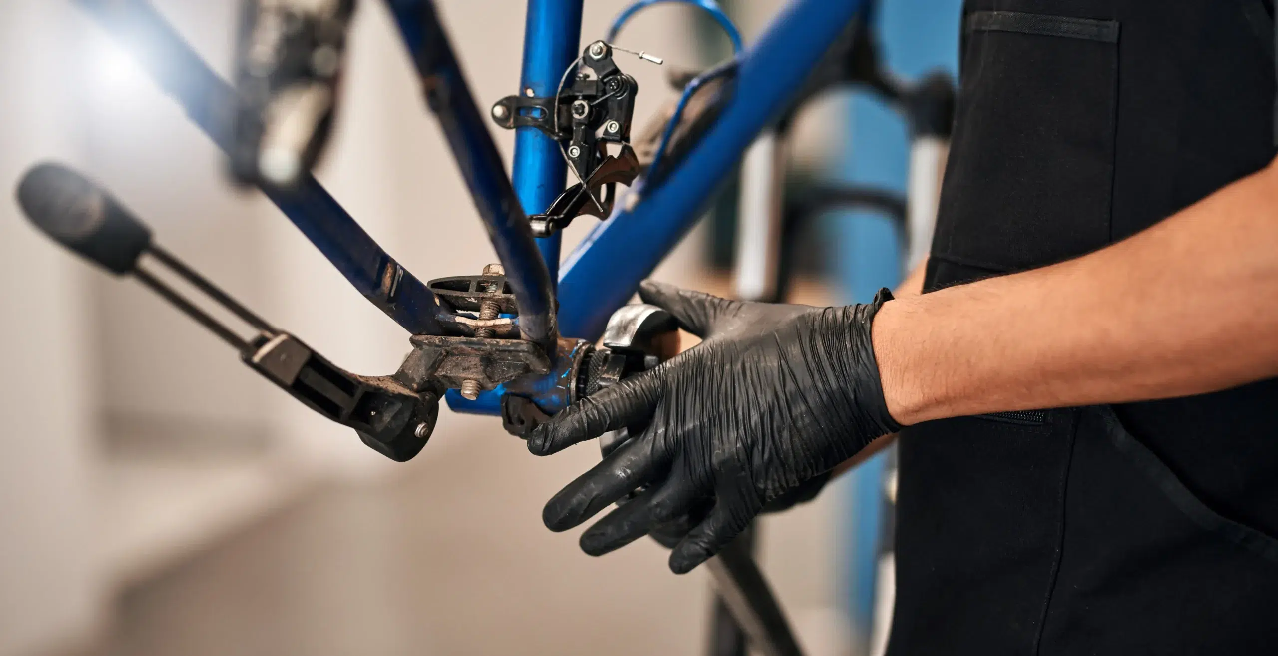 Person mit schwarzen Handschuhen repariert einen blauen Fahrradrahmen.