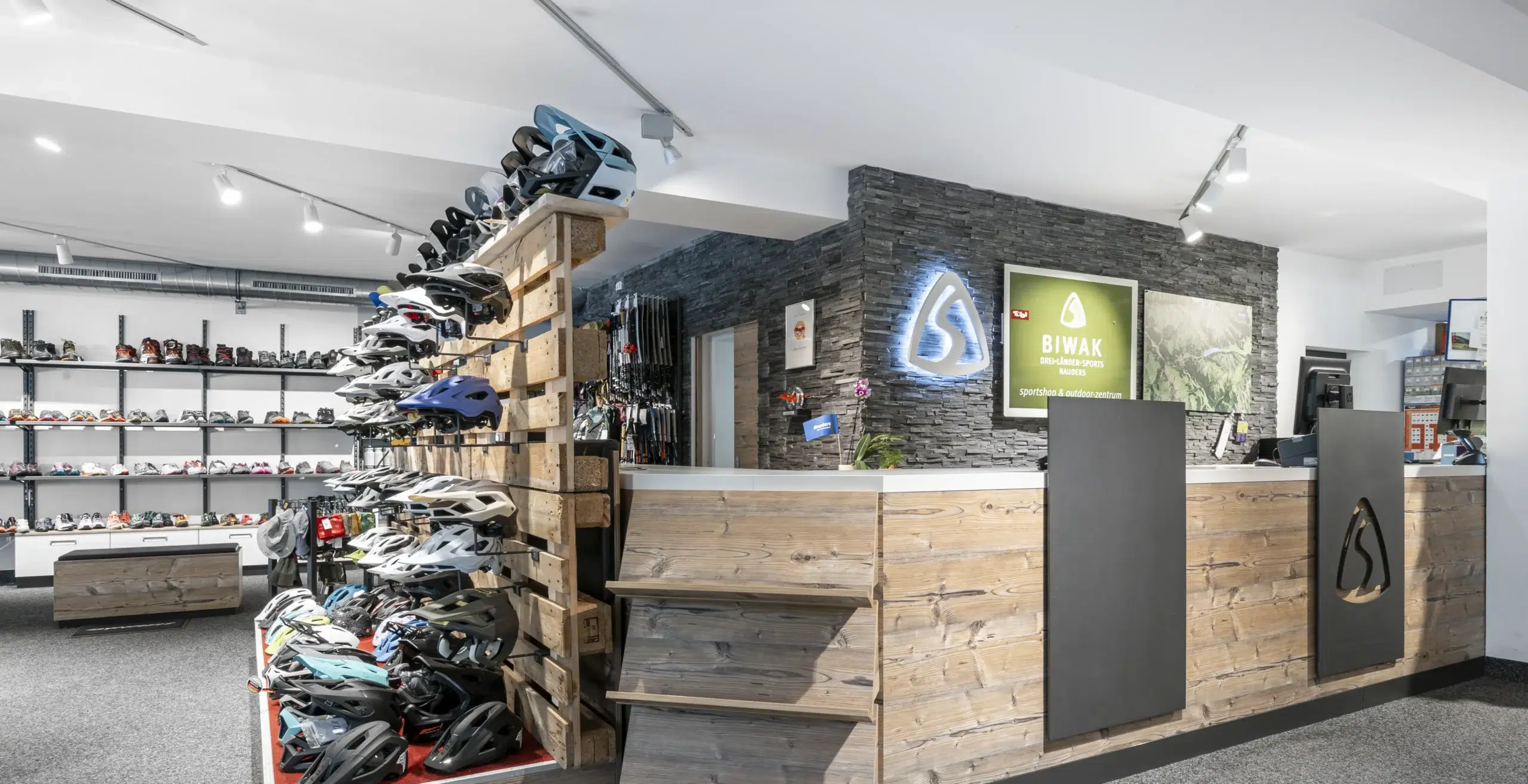 Modernes Interieur eines Fahrradladens mit Helmen auf Holzregalen und an den Wänden ausgestellter Ausrüstung.