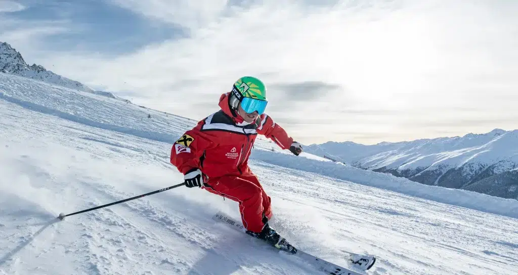 Skifahrer in rotem Anzug und grünem Helm beim Skifahren auf einem verschneiten Berghang.