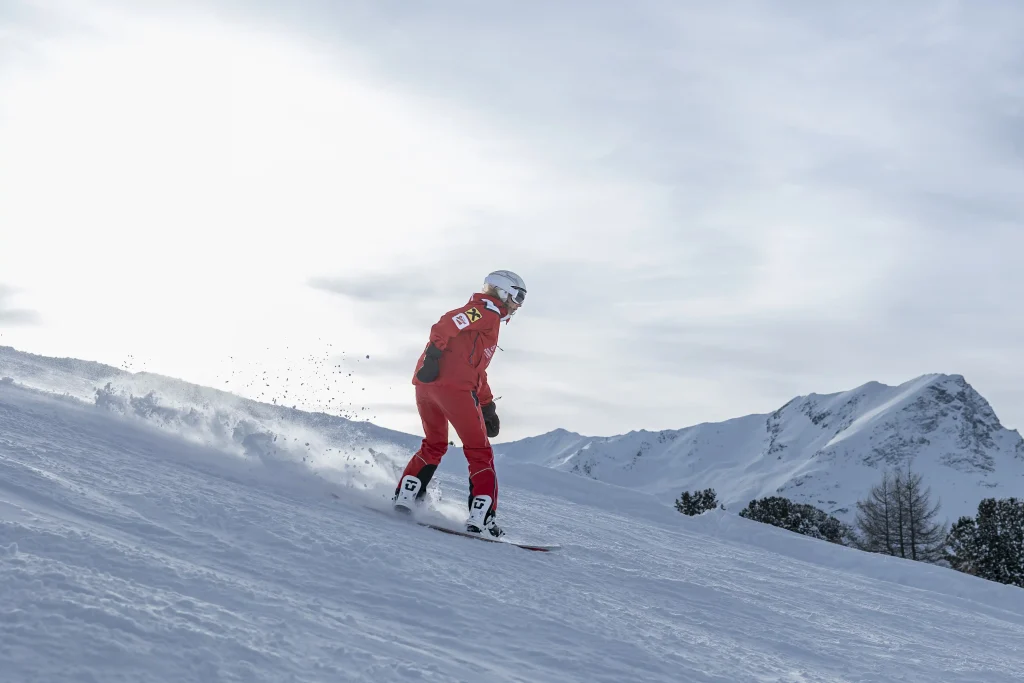 Skifahrer im roten Anzug fährt eine verschneite Piste mit Bergen im Hintergrund hinunter.