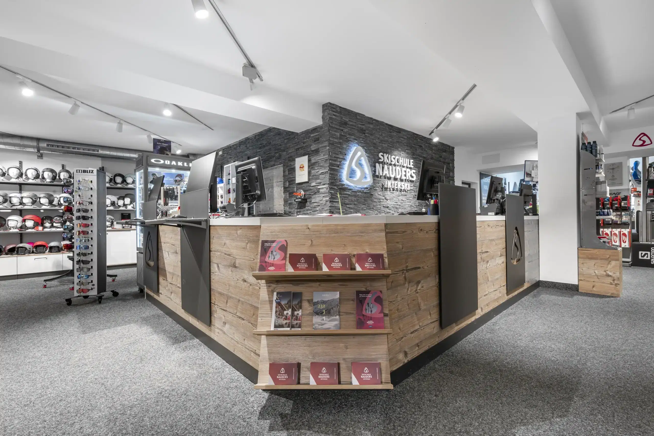 Modernes Skigeschäft mit Holztheke, Prospekten, Helmen und Ausrüstungsgegenständen in den Regalen.