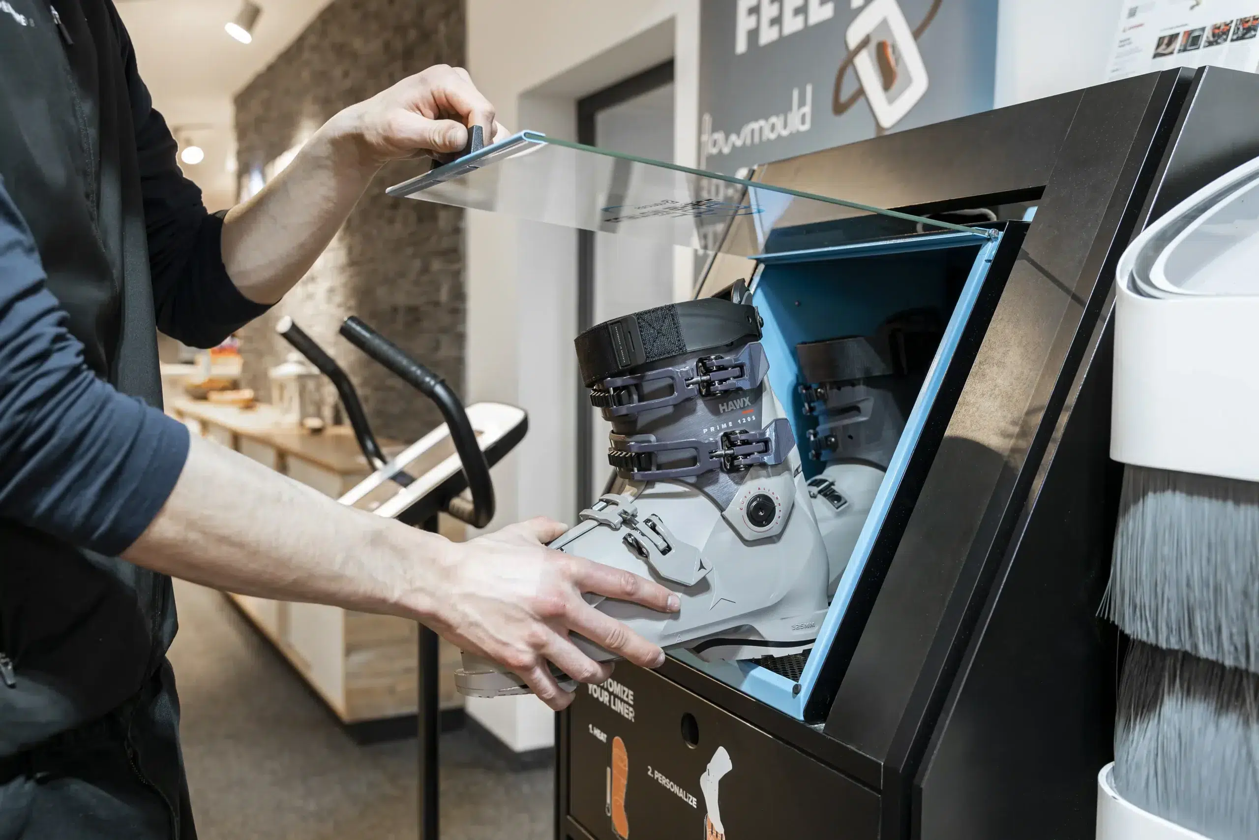 Person, die einen Skischuh in einen Skiverleih-Automaten mit Glasdeckel in einem Geschäft einlegt.