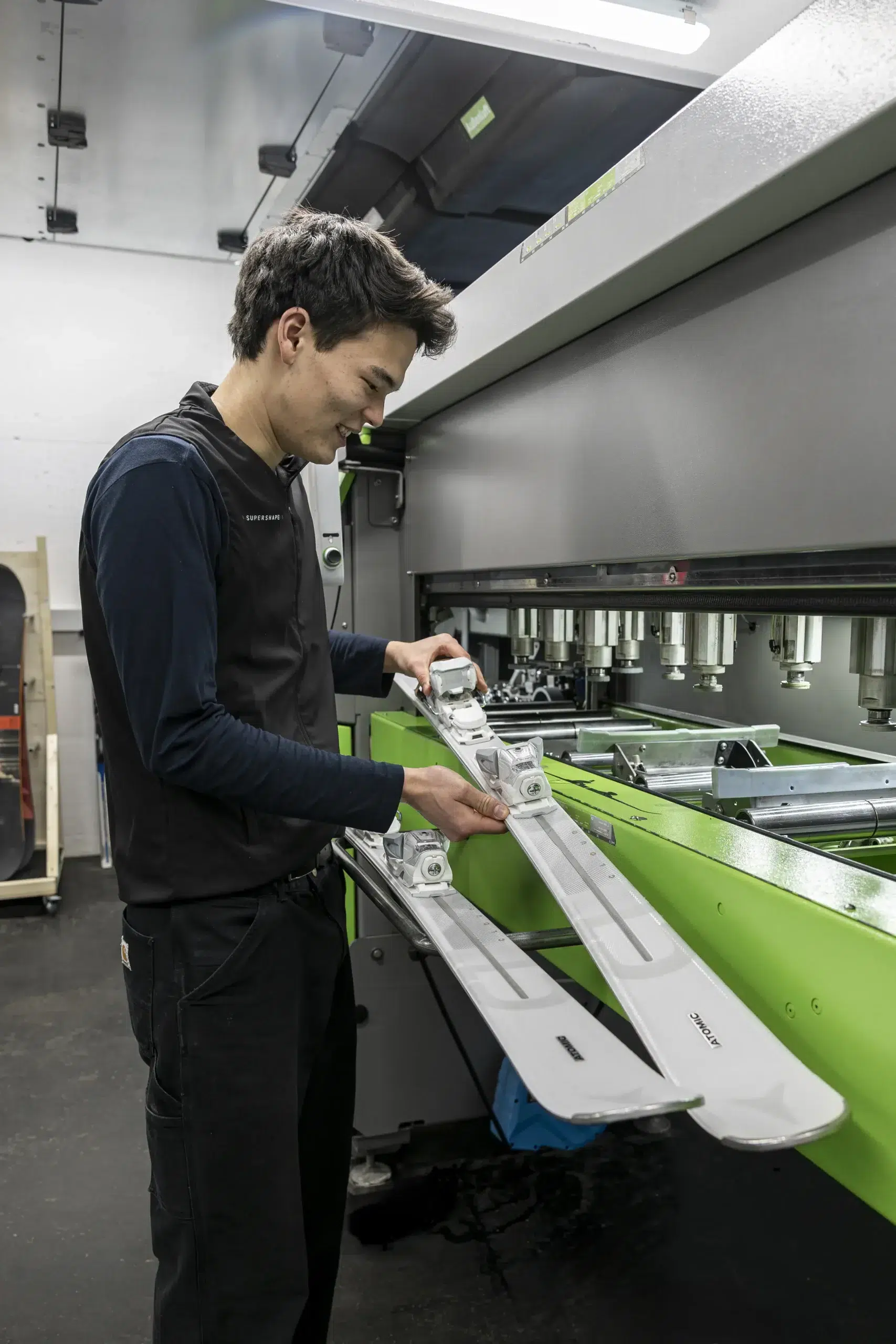 Ein Mann inspiziert ein Paar Skier an einer Maschine in einer Werkstatt.