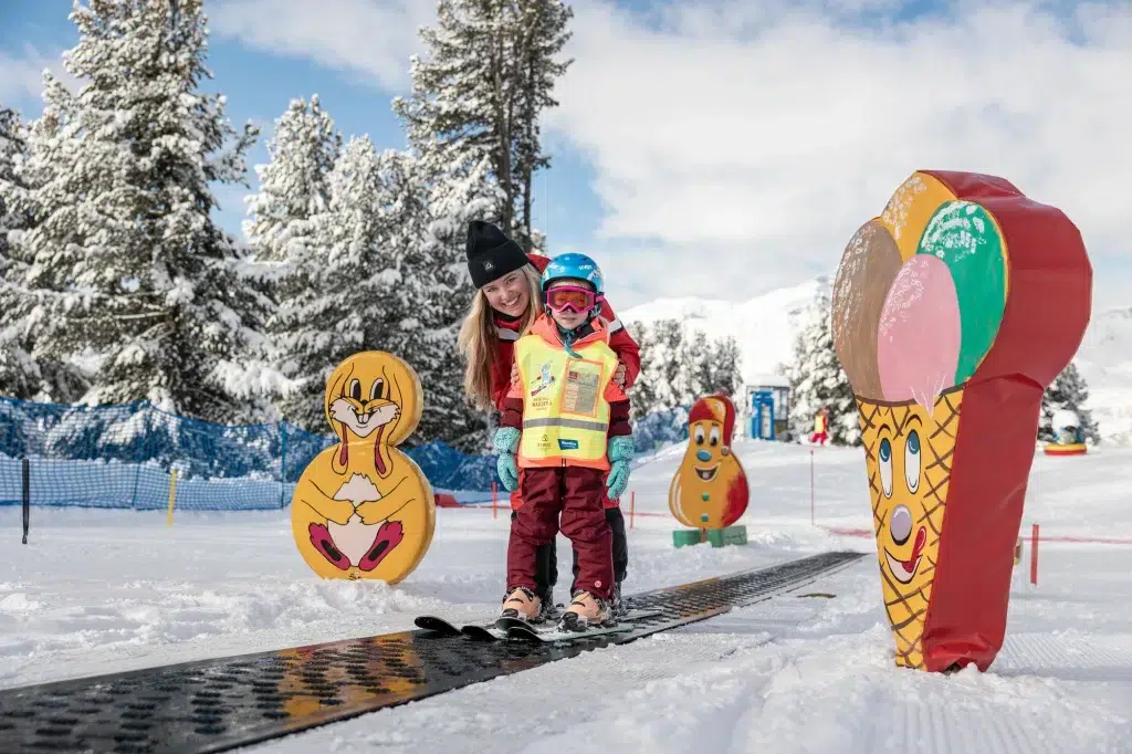 Ein Kind lernt mit einem Erwachsenen zwischen bunten Cartoon-Dekorationen im Schnee das Skifahren.