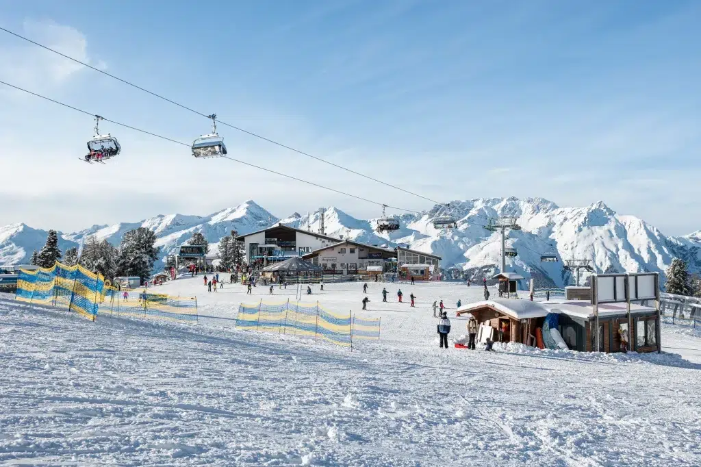 Skifahrer auf verschneiten Pisten mit Sesselliften und Bergen im Hintergrund an einem sonnigen Tag.