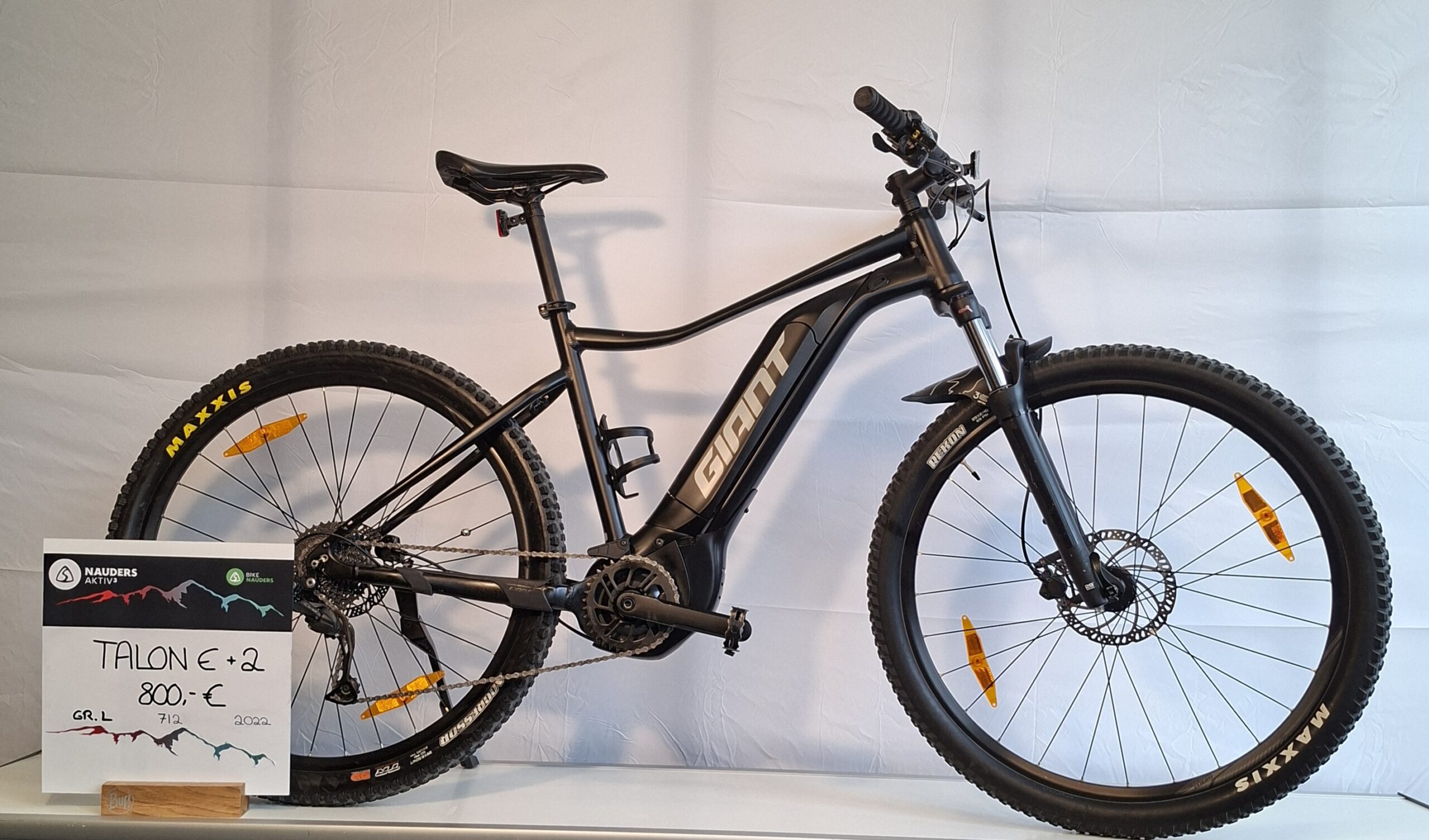 Giant Talon E + 2 Mountainbike mit Scheibenbremsen von einem weißen Info-Schild auf einem Ständer gezeigt.