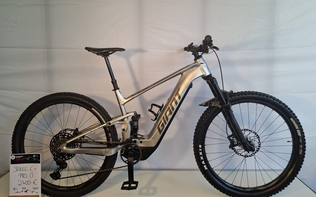 Silbernes Giant-Mountainbike mit dicken Reifen, das in einem Innenraum vor einem weißen Hintergrund ausgestellt ist.