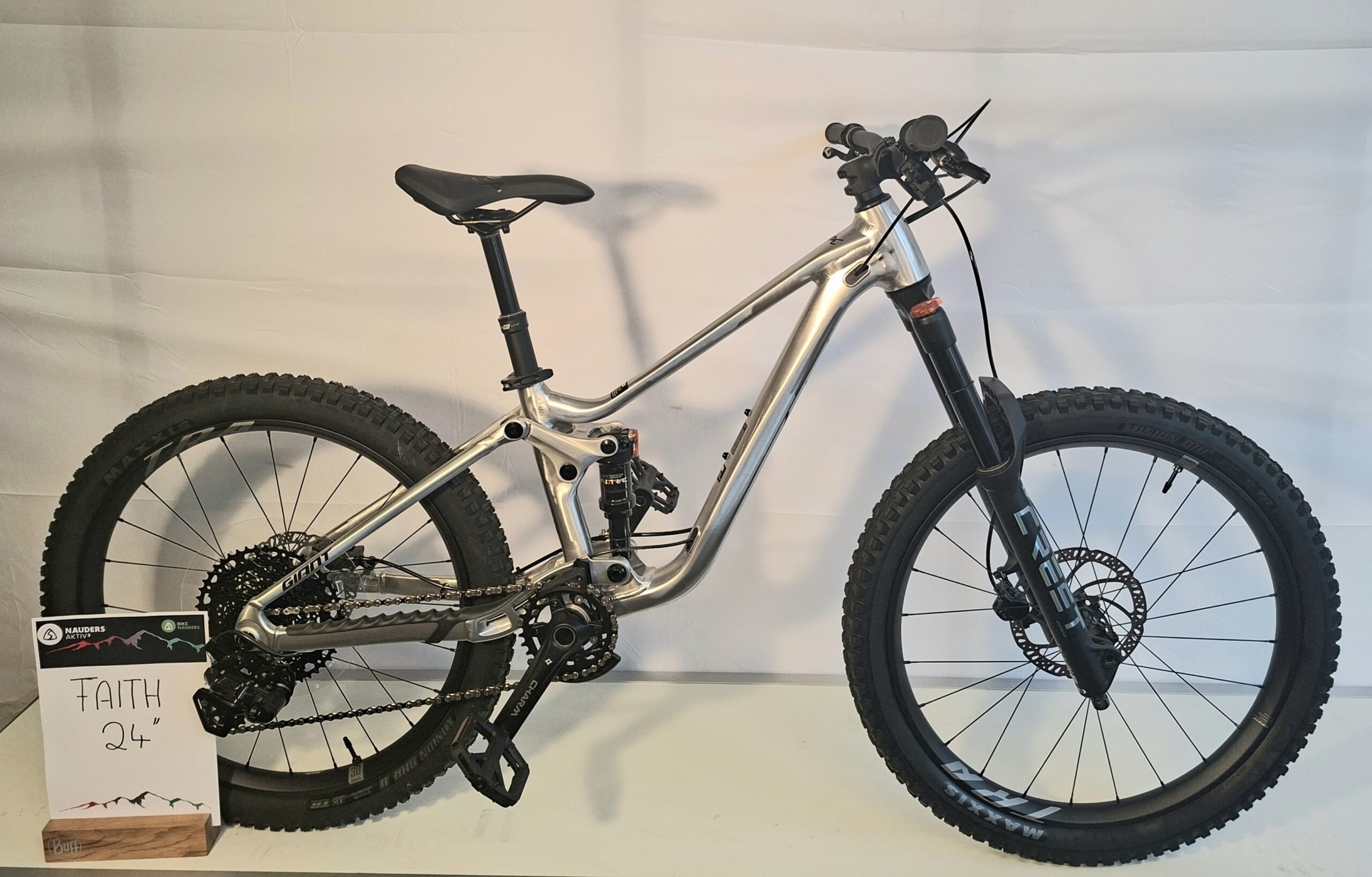 Ein silbernes Mountainbike Faith 24 mit dicken Reifen steht neben einem Schild mit der Aufschrift FAITH 24.